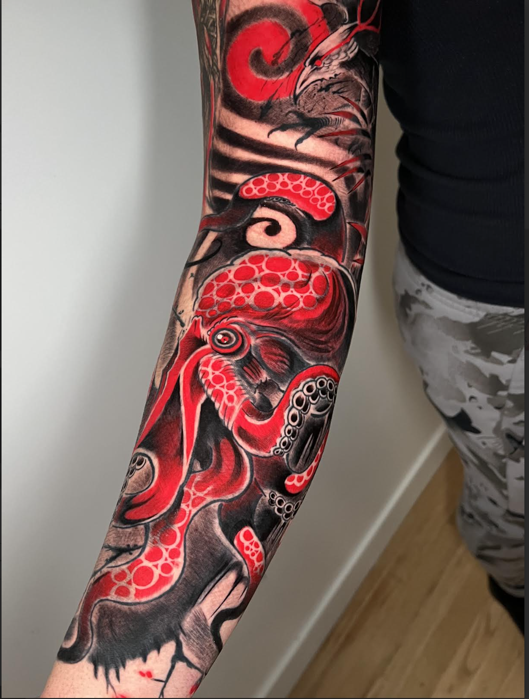 Dense color forearm tattoo with a red octopus, ideal cover-up style