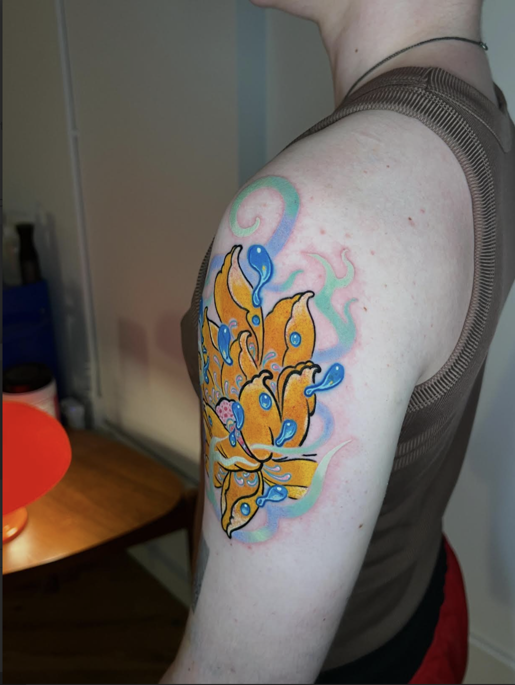 Vibrant yellow and orange lotus color tattoo on a shoulder